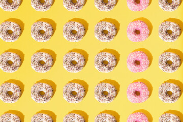 Arranged small ring donuts with white and pinl glaze. Colorful crumbs on a yellow pastel background. Pattern. Flat lay.