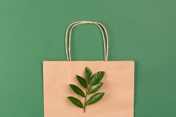 Recycled kraft paper bag with green leaves on green background. Sustainable shopping packaging concept. Green shopping