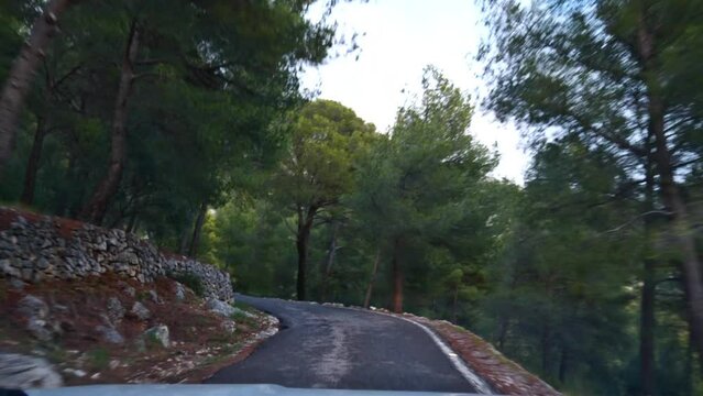 Front view of car driving on narrow curvy road to the peak of mountain Mont Faron near Toulon, France at the French Riviera with rocks and green trees passing by.