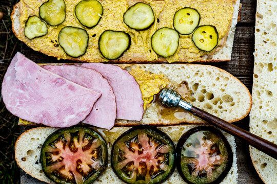 sandwich preparation with ham slices, mustard, pickles, honey dipper and drizzled honey over black heirloom tomato slices