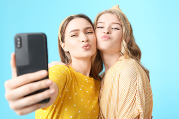 Portrait of grimacing young sisters taking selfie on color background