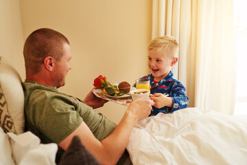 Serving breakfast to the best Dad ever. Cropped shot of a little boy serving breakfast in bed to...
