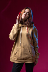 Young beautiful fashionable hipster girl dressed in a hoodie  listening to music in red headphones in a studio red dramatic background