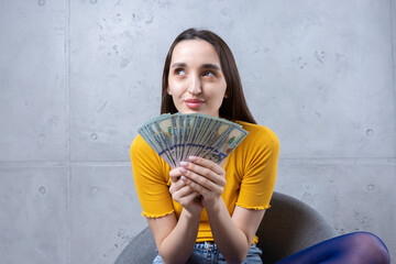 Photo of a wealthy woman in simple clothes holding a fan of dollar money isolated against a concrete wall background