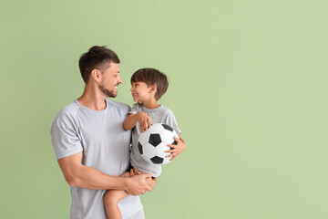 Male trainer with little boy and ball on green background