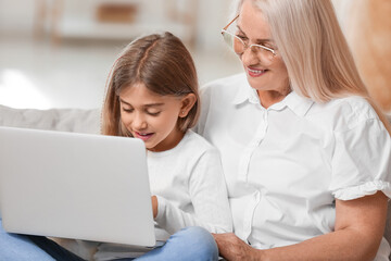 Little girl with her grandma using laptop on sofa at home