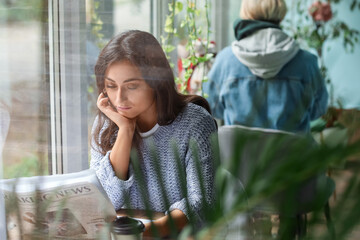 Beautiful young woman reading newspaper at table in cafe