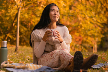 Portrait of cute girl sitting and having a cup of tea in a park picnic dressed fashionable on a...