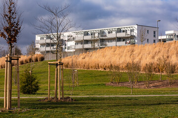 Ein Neubau Wohnblock vor dunklen Wolken und einer Grünfläche als moderner menschlicher Lebensraum
