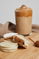 Argentine white chocolate alfajores, cold coffee, frappe and spoon with dulce de leche on a wooden board on a marble table with a kitchen towel.