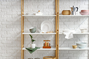 Modern shelf units with kitchenware near white brick wall