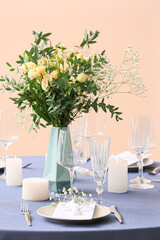 Stylish table setting with wedding invitation and gypsophila flowers near beige wall