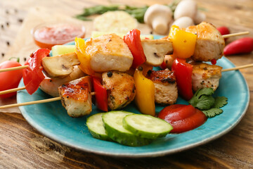 Plate of grilled chicken skewers with vegetables on wooden background