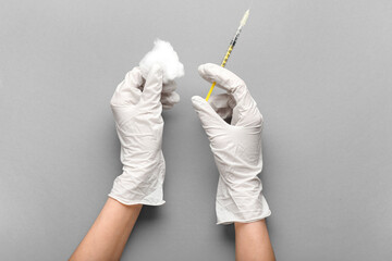 Female hands in rubber gloves with syringe and cotton wool on grey background, closeup