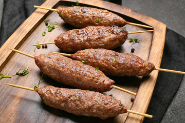 Wooden board of skewers with tasty lula kebab on table