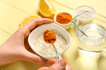 Woman making turmeric mask on color wooden background, closeup