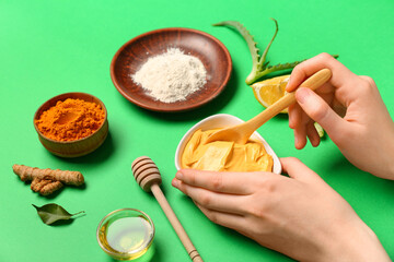 Woman stirring turmeric mask in bowl on green background, closeup