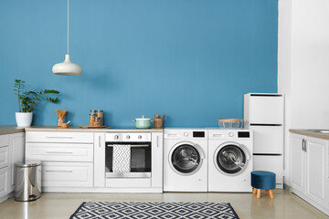 Interior of stylish kitchen with modern washing machines, oven and white counters