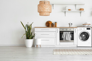Interior of light kitchen with washing machine, oven and white counter