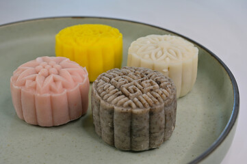 Four mini snow skin mooncakes with floral & Chinese 'wanzi' imprints on a green serving plate