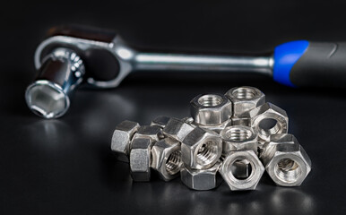 Stainless steel hexagon nuts pile with reflection and ratchet wrench on black background. Closeup of metal hex fasteners with threaded hole on heap or blurry socket spanner hand tool. Tech still life.
