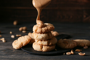 Pouring of peanut butter onto tasty cookies on black wooden background