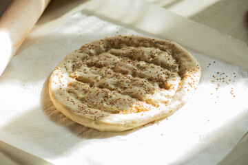 Round piece of dough on a table, preparing Ramadan pide with sesame seeds. - 490787578