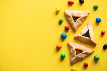 Top view of hamantaschen cookies and colorful candies on yellow background. Copy space. - 490787579