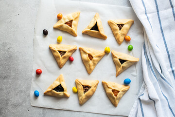 Fototapeta na wymiar Top view hamantaschen cookies and colorful candies on a baking paper with napkin on a gray background.