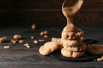 Pouring of peanut butter onto tasty cookies on black wooden background