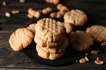 Board with tasty peanut cookies on black wooden background