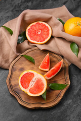 Board with tasty cut grapefruit on dark background