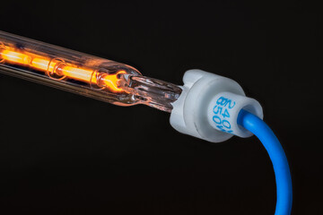 Detail of hot resistance wire in hollow glass tube with blue cable on a black background. Flow of...