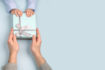 a father receives a gift box with a bow from the hands of his child in close-up