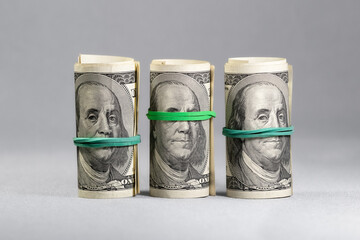 A set of three rolls of hundred-dollar bills stretched with an elastic band. The concept of the...