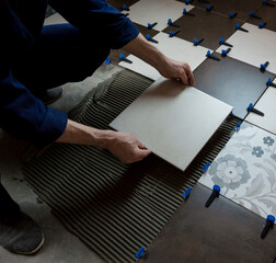 A worker glues ceramic tiles on the floors.