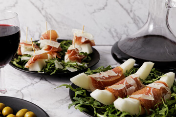 Tapas from Serrano ham and melon on arugula with cheese flakes snack salad with red wine.