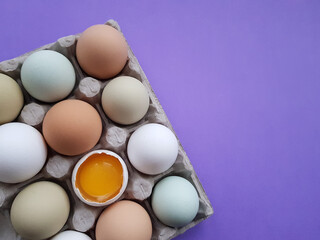 farm eggs are natural colored in an egg tray on a lilac background color 2022. one is broken