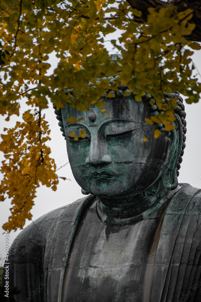 Sticker Vertical shot of buddha statue behind yellow leaves in Japan