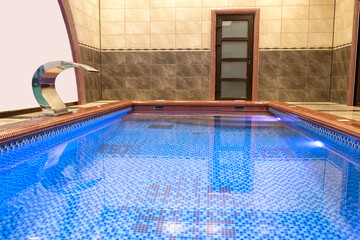 Illuminated pool with waterfall, sauna entrance, indoor blue pool