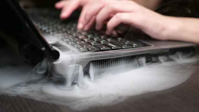 A close-up of an old laptop falling apart with smoke coming out of it. Short circuit and death of an old computer