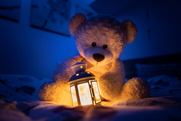 Closeup shot of the teddy bear toy and night light on the bed in the dark