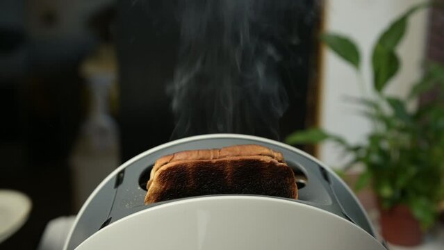 Burnt slices of bread fly out of the toaster, which is smoking. Toast burnt due to broken old toaster. bad morning