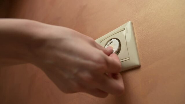 Woman inserts plugs into power outlet to protect children from electric shock. Close up