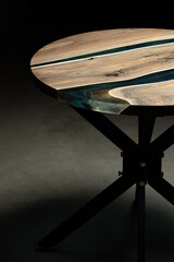 Fototapeta na wymiar Expensive vintage furniture. The table is covered with epoxy resin and varnished. Luxury quality wood processing. Wooden table on a dark background. A blue epoxy river in a round tree slab.