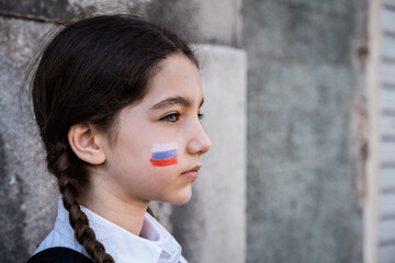 Obraz na płótnie Canvas Portrait of a sad child girl with Russian colors on face. Peace and protection children concept