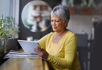 Technology helps her keep in touch with friends. Shot of a mature woman using a digital tablet in a coffee shop.