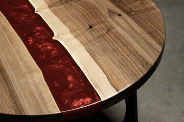 Expensive vintage furniture. The table is covered with epoxy resin and varnished. Luxury quality wood processing. Wooden table on a dark background. A red epoxy river in a round tree slab.
