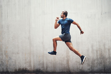 Fototapeta na wymiar Keep up the energy. Shot of a sporty young man running against a grey wall outdoors.
