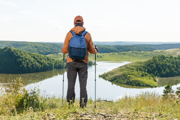 Man solo traveling backpacker hiking in  mountains. Tourist stands near lake enjoying the sunset, thinking.